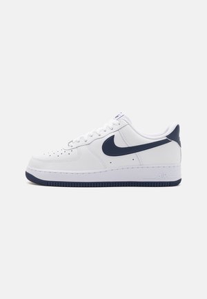 Weißer Sneaker mit niedrigem Schaft, dunkelblauem Nike-Swoosh, dunkelblauem Fersenlasche und dunkelblauem Sohlenrand, geschnürt und von der Seite gezeigt.