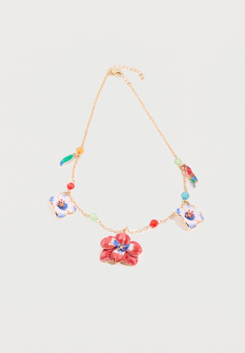Collier en chaîne dorée avec breloques en forme de fleurs rouges et blanches, petits perles colorées et deux pendentifs en forme d'oiseaux sur fond blanc.