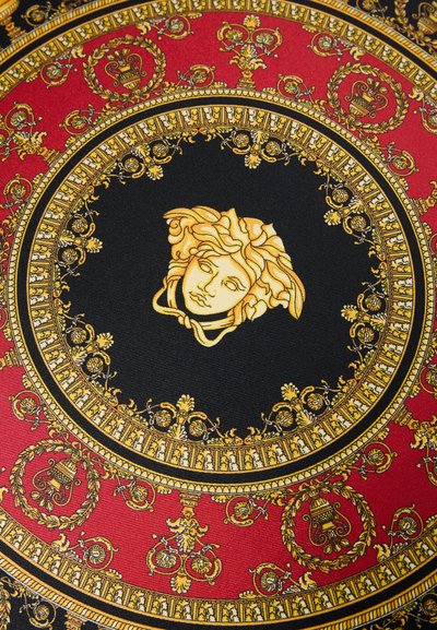 Kerek szövettextil részletes aranymintákkal fekete alapon, piros szegéllyel kiemelve és középen egy arany Medúza-fej díszítéssel.