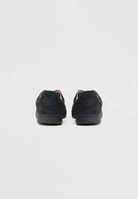 Zapatillas de ante negras con textura suave, punta redonda y suelas de goma. Diseño minimalista con detalles cosidos y perfil bajo.