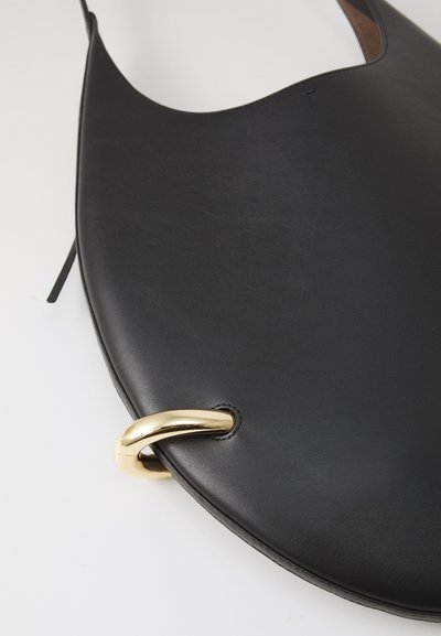 Melnas ādas rokassomi ar gludu, izliekta dizaina. Tam ir izteiksmīgs zelta metāla gredzens un smalks šuvums tuvu malai.