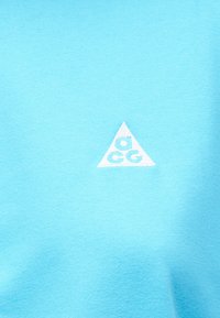 Ανοιχτό μπλε ύφασμα με μικρό λευκό τριγωνικό λογότυπο στο κέντρο που διαθέτει στυλιζαρισμένα γράμματα "a," "c," και "g".