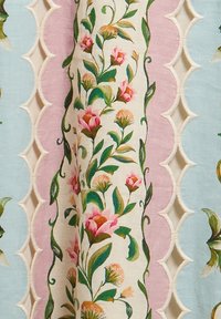 Κάθετες ανθισμένες ρίγες με ροζ και πορτοκαλί λουλούδια, πράσινα φύλλα σε κρεμ φόντο, περιτριγυρισμένες από ροζ και μπλε κυματοειδείς άκρες με κομμένα διαμαντένια σχήματα.