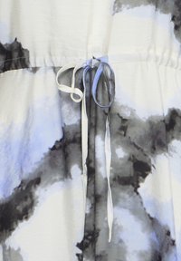 Cordon noué en forme de nœud sur un tissu à motif tie-dye abstrait en noir, blanc et gris, montrant le détail de la taille froncée.