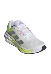 Zapatilla deportiva blanca con rayas grises, toques en rosa y verde neón, y parte superior de malla texturizada. Cuenta con una suela negra y una punta reforzada.