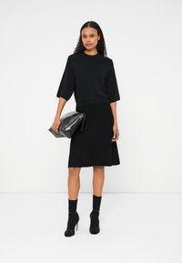 Fekete kötött ruha rövid ujjakkal, testhezálló derékkal és bővülő szoknyával. Fekete clutch táskával és bokazoknival, magassarkúval párosítva.