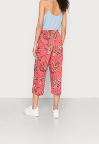 Korallfärgade culottbyxor med blommönster, elastisk midja och kort längd, kombinerade med vita sneakers och en ljusblå ärmlös topp.