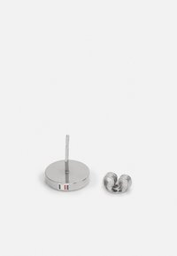 Sølv metalløreringstativ med en rett stang og rund base, med rød, hvit og blå akcent. Inkluderer en spiralformet øredesign.