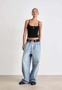 Must kaugus tank top musta värviga, millel on reguleeritavad rihmad ja esiosa logo detail, koos helesiniste ülemõõduline teksapükstega, millel on nööriga vöö.
