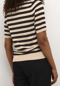 Strikket kortærmet top i beige og sorte striber; tætsiddende design med ribbede manchetter og kant. Synlig tekstur og fleksibelt stof.