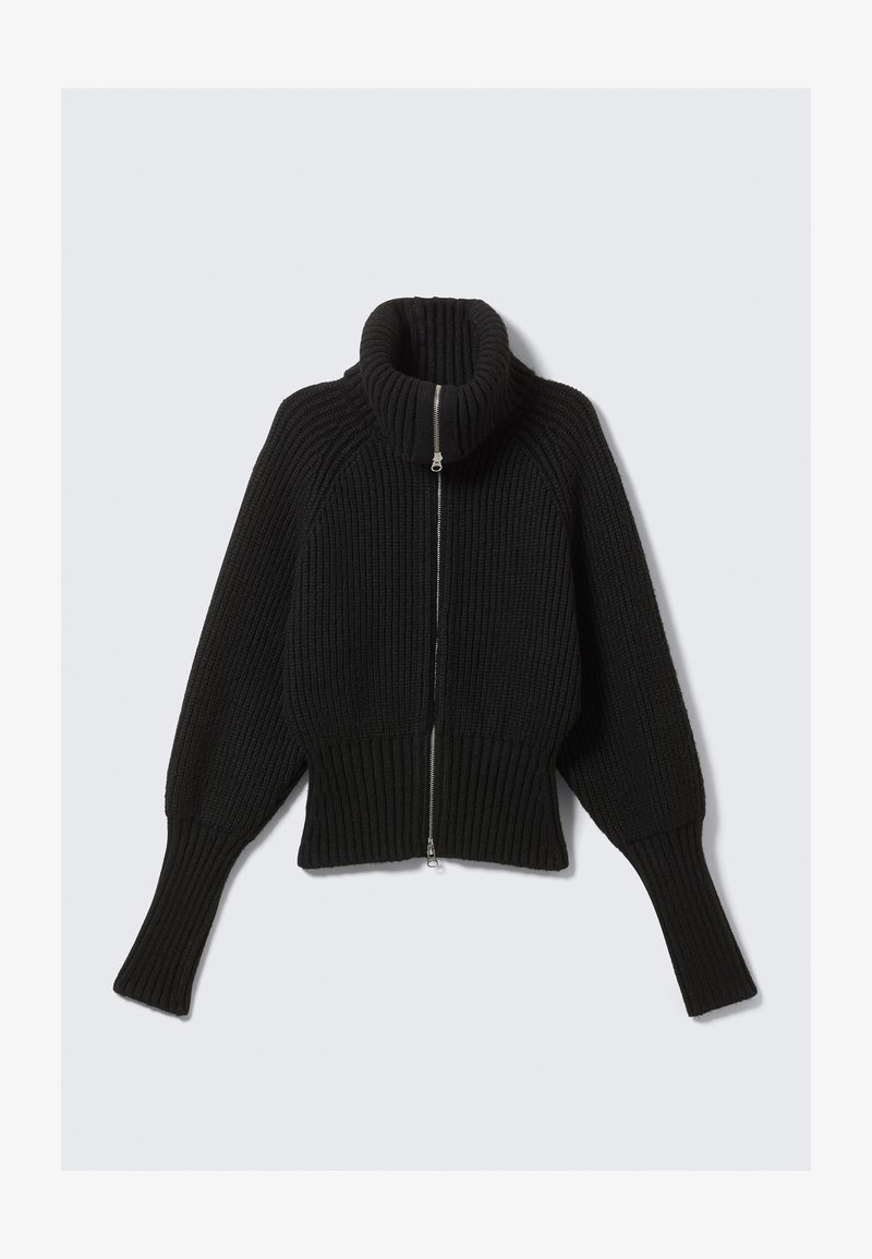 Pull en tricot noir à côtes, avec un col montant et une fermeture éclair sur le devant ; présente des manches larges et un ourlet court. Texture douce sur l'ensemble.