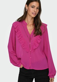 Langarm, pinke Bluse mit einem strukturierten Punktmuster, mit gerafften vorderen Kanten und einem Knopfverschluss. Leichter Stoff.