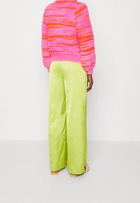Maglione fuzzy rosa e arancione a righe con scollatura rotonda, abbinato a pantaloni satinati verde brillante a gamba larga con spacchi laterali.