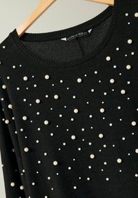 Maglione nero lavorato a maglia con scollatura rotonda, decorato con pietre di vetro bianche di diverse dimensioni disposte sul tessuto.