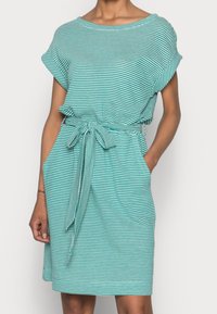 Raitaneita turkoosi mekko, jossa on lyhyet hihat, vyötä oleva vyötärö ja solmittava vyö. Sisältää sivutaskut ja rento istuvuus. Pehmeä kankaan rakenne.