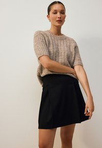 Pull en tricot côtelé beige à manches courtes, associé à une jupe noire à coupe droite avec des plis sur le devant. Design simple, sans motifs.