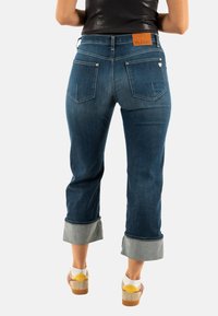 Jeans de mezclilla azul con corte recto, puños doblados y una etiqueta de cuero que dice "PLEASE" en la parte posterior. Presenta dos bolsillos traseros.