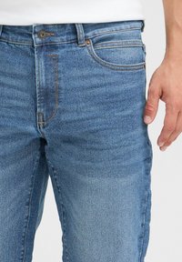 Vaqueros de denim azul con un corte clásico, un ligero desgaste, costuras en contraste y un cierre de botón único en la cintura.