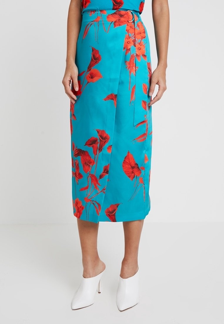 Gonna midi turchese con stampa floreale rossa. Presenta un design avvolgente e una consistenza liscia. Abbinata a scarpe col tacco alte bianche.