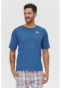 Niebieski T-shirt z krótkim rękawem, wykonany z miękkiego materiału, z małym pomarańczowym nadrukiem psa na piersi. W połączeniu z kratkowymi piżamami.