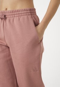 Pantaloni da jogging in felpa rosa con cintura elastica e cordoncino; tasche laterali; presenta un logo ricamato sulla gamba.