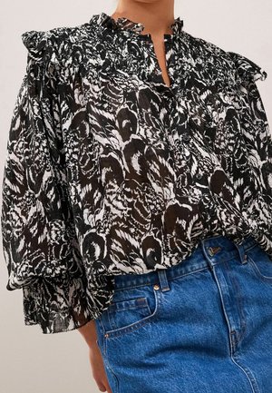 Zwart-wit bloemenpatroon doorschijnende blouse met gerimpelde schouders, gecombineerd met hooggesloten blauwe spijkerbroek.