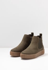 Olivgröna ankelskottar i mocka med slät yta, elastiska sidopaneler, dragkedjestängning och en kraftig brun gummisula.