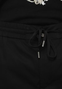 Black shorts made of smooth material with an elastic waistband, drawstring with metal tips, and stitching details along the edges.