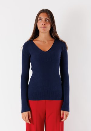 Maglione a maniche lunghe ribbed in navy con design a V; forma aderente e tessuto testurizzato; abbinato a pantaloni rossi.