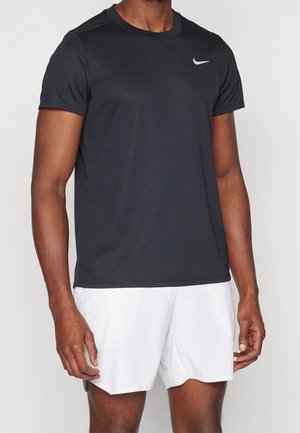 Man wearing black short-sleeve Nike sports shirt and white athletic shorts standing against a plain background.