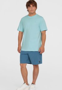 Svetlo modra bombažna majica s kratkimi rokavi in okroglim izrezom, v kombinaciji s srednje modrimi kratkimi hlačami in belimi tenisicami.