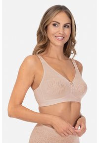 Beżowy materiałowy stanik bezprzewodowy z dekoltem w kształcie V, kwiatowymi wzorami, szerszymi ramiączkami oraz centralnym akcentem z ozdobnym zapięciem.