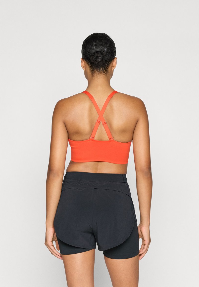 Rode sportbeha met kruislings straps, gecombineerd met zwarte sportshorts met een gelaagd ontwerp en een gladde textuur.