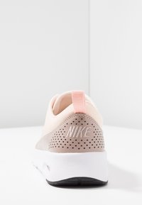 Nike footwear featuring a light pink fabric upper, tan accents, and perforated detailing. White midsole with black rubber outsole; pull tab at heel.
