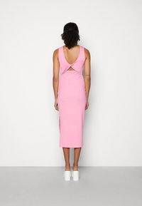 Vestido midi rosa com costas profundas e detalhes torcidos. Feito de um tecido suave, apresenta fendas laterais e é usado com saltos bloco brancos.