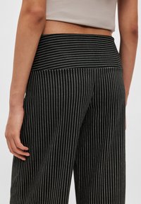 Czarno-białe spodnie o szerokich nogawkach w paski z elastycznym pasem. Tkanina wydaje się gładka z delikatnym połyskiem i pionowym wzorem.