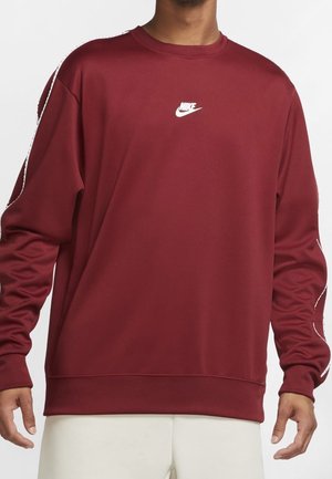 Mørkerød Nike-sweatshirt med hvidt logo på brystet og hvide mærkede striber langs ærmerne, båret af en person med lyse bukser.