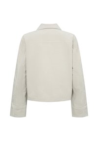 Beige kordjacka med spetsig krage, långa ärmar och cropped design. Bakifrån syns platta sömmar och texturerat tyg.