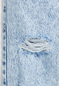 Helles blaues Denim-Gewebe mit einem abgenutzten Patch und ausgefransten Kanten, der in der Mitte einen Riss erzeugt. Subtile Textur mit verblassten Mustern.