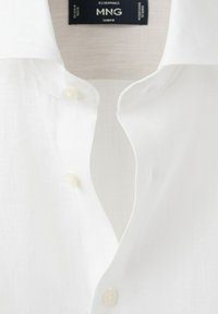Weißes Hemd mit Knopfleiste, weiter Kragen und schwarzem "MNG Essentials"-Etikett im Nackenbereich.