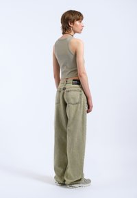 Top corto de color verde oliva claro y jeans de tiro alto, holgados. Los detalles notables incluyen una mínima marca y un tejido texturizado.