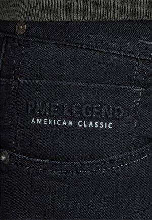 Nahaufnahme einer schwarzen Jeans-Tasche mit dem eingeprägten Text "PME Legend" und dem aufgedruckten Text "American Classic".