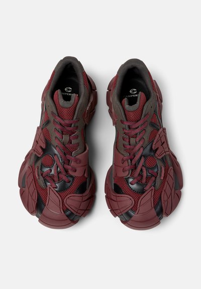 Klobige Sneaker in Burgunderrot und Schwarz mit strukturiertem Mesh, mehrfach geschichteten, geformten Sohlenakzenten und gemusterten Schnürsenkeln, von oben auf weißem Hintergrund gesehen.