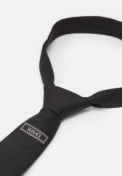 Schwarze Fliege aus glattem Stoff mit geripptem Muster. Verfügt über ein graues, auf der Unterseite genähtes "VERSACE"-Etikett. Klassisches Design und Form.