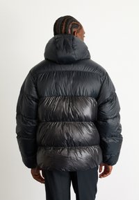 Sort pufjakke med en stor, rund hætte, skinnende, quiltet tekstur og en cropped, overdimensioneret pasform. Ærmerne er let indsnævret.
