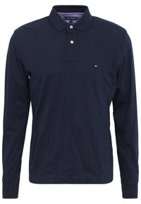 Námořnická modrá polokošile s dlouhým rukávem a límečkem, s dvouknoflíkovou légou a malým červeným, bílým a modrým logem na levém prsu.