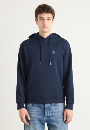 Donkerblauwe hoodie van een katoenmix, met een voorzak, trekkoorden en geborduurd logo op de borst. Casual pasvorm.