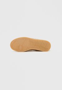 Braune Gummisneaker sohle mit strukturiertem Muster und kreisförmiger Markenprägung; hellbraune Farbe mit glatter Oberfläche.