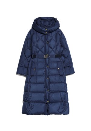 Femme portant un long manteau matelassé bleu marine avec capuche, taille cintrée avec ceinture, boutons dorés, mains dans les poches, associé à des bottes noires.