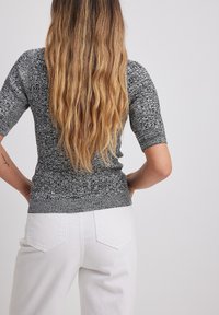 Top grigio a maniche corte lavorato a maglia con un motivo testurizzato, vita aderente e materiale morbido. Abbinato a jeans bianchi a vita alta, visto da dietro.